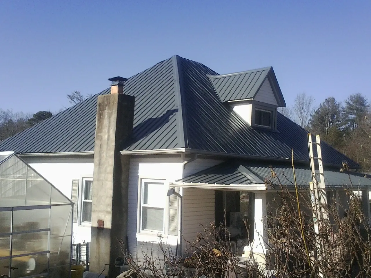 Dark blue standing seam metal roof on a white farmhouse with dormer — Slate & Tile Roof Repair by Roofing Brothers in Steinhatchee