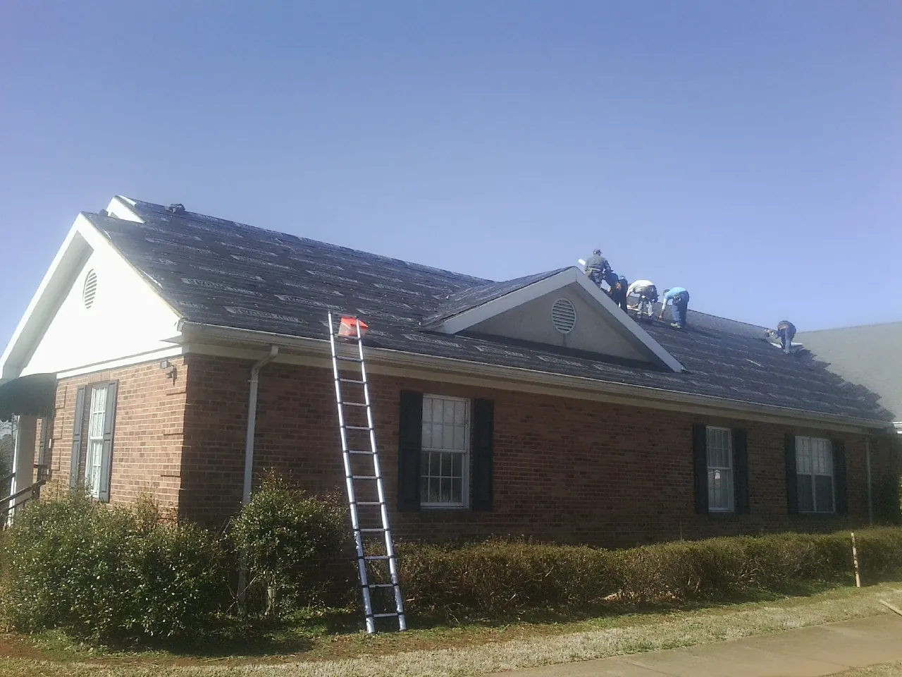 Crew tearing shingles off a brick ranch roof with a ladder set — Metal Roof Repair work by our crew in Steinhatchee